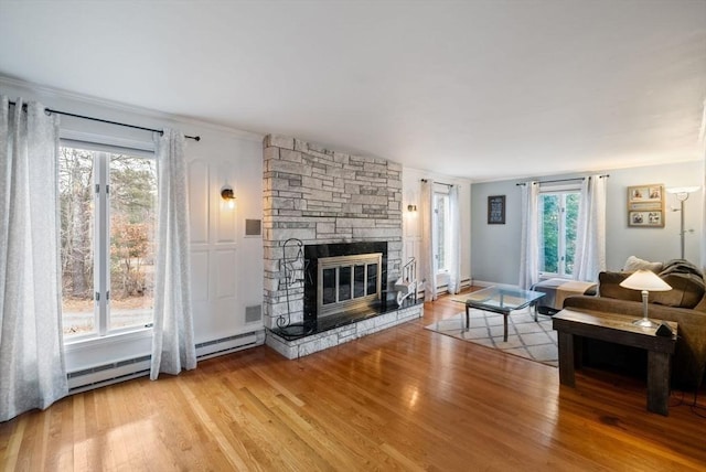 living room featuring light wood-type flooring, a wealth of natural light, a baseboard heating unit, and a fireplace