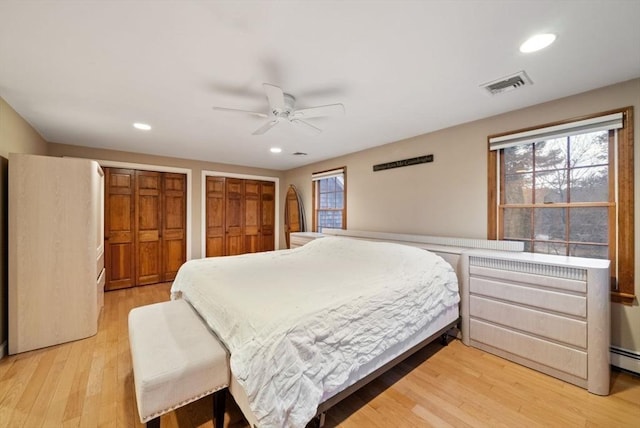 bedroom featuring multiple closets, light hardwood / wood-style floors, and ceiling fan