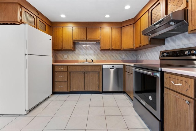 kitchen with appliances with stainless steel finishes, under cabinet range hood, a sink, brown cabinets, and light countertops