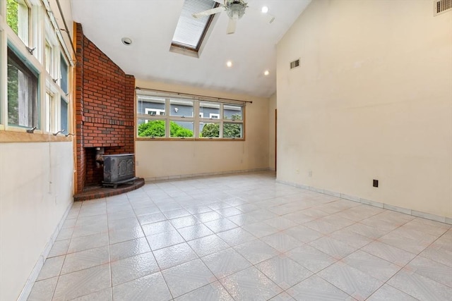 spare room with a wood stove, ceiling fan, high vaulted ceiling, baseboards, and a skylight