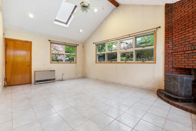 empty room featuring high vaulted ceiling, a wood stove, a ceiling fan, beamed ceiling, and a skylight