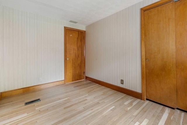 empty room with wood finished floors, baseboards, and wallpapered walls