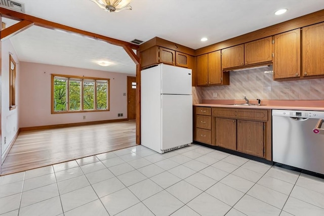 kitchen featuring freestanding refrigerator, dishwasher, a sink, light countertops, and brown cabinetry