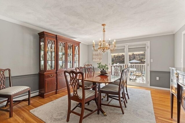 dining space with a textured ceiling, crown molding, baseboard heating, light wood-type flooring, and a chandelier