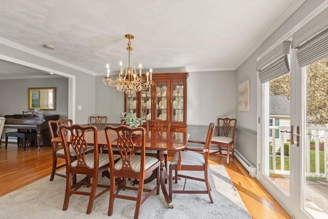 dining area with a notable chandelier, ornamental molding, baseboard heating, and light wood-type flooring