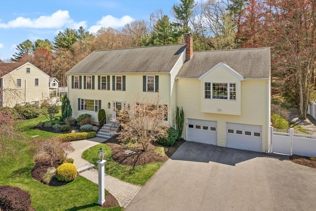 colonial inspired home featuring fence, a shingled roof, an attached garage, a chimney, and driveway