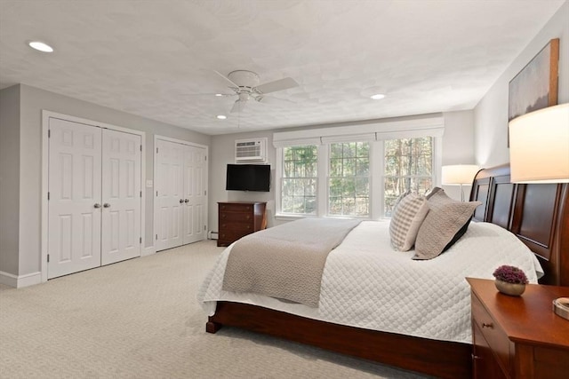 bedroom with light colored carpet, recessed lighting, baseboards, and two closets