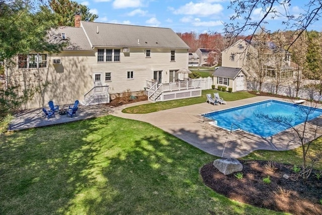 outdoor pool with a lawn, a wooden deck, an outbuilding, fence, and a patio