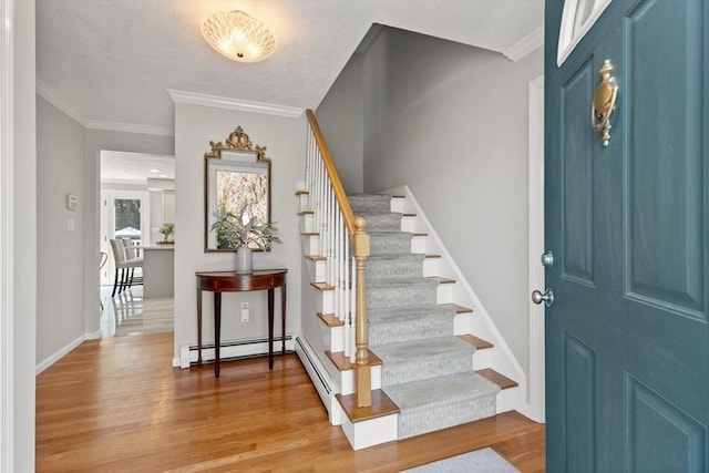 entrance foyer featuring ornamental molding, wood finished floors, baseboard heating, and stairway