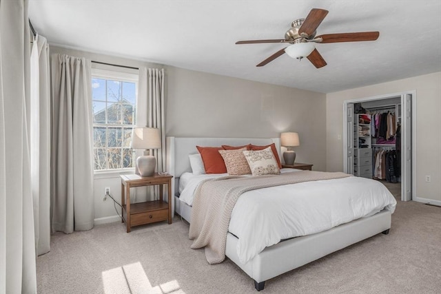 bedroom featuring light colored carpet, a ceiling fan, baseboards, a closet, and a walk in closet