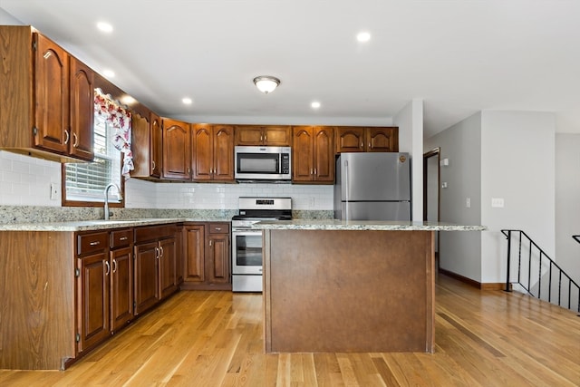 kitchen with a kitchen island, light hardwood / wood-style flooring, stainless steel appliances, light stone countertops, and backsplash