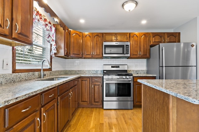 kitchen with light stone counters, sink, stainless steel appliances, and light hardwood / wood-style floors