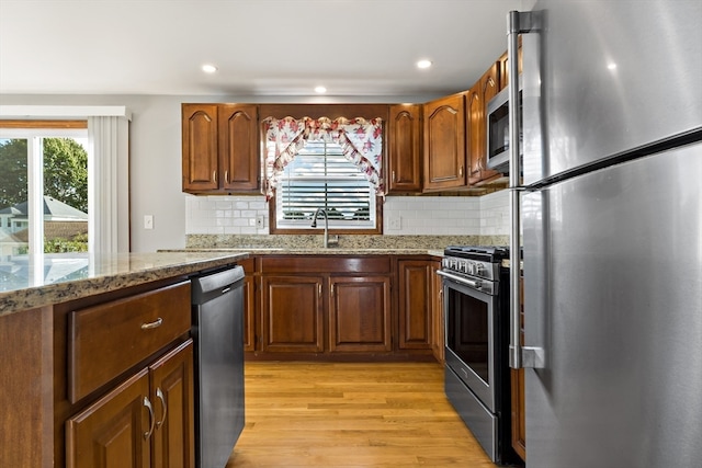 kitchen with light wood-type flooring, light stone counters, stainless steel appliances, and backsplash