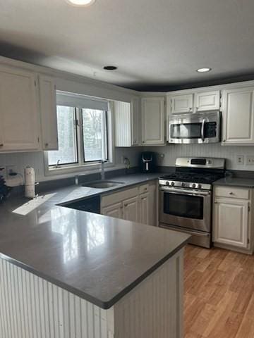 kitchen featuring dark countertops, appliances with stainless steel finishes, light wood-style floors, a sink, and a peninsula