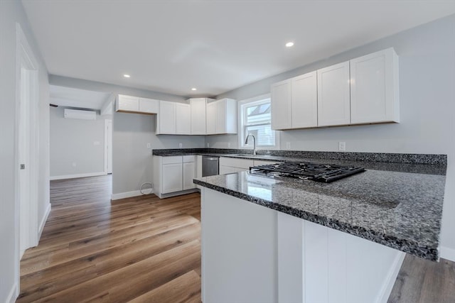 46 Lyons St, Lowell, MA 01852 - kitchen featuring a peninsula, dark stone counters, a wall mounted air conditioner, white cabinetry, and a sink
