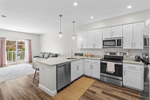 kitchen with a sink, a peninsula, open floor plan, stainless steel appliances, and white cabinetry