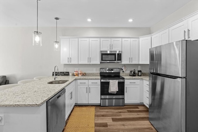 kitchen featuring a peninsula, wood finished floors, white cabinets, a sink, and appliances with stainless steel finishes