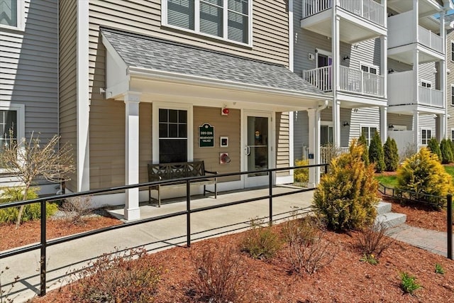 doorway to property featuring a porch and a shingled roof