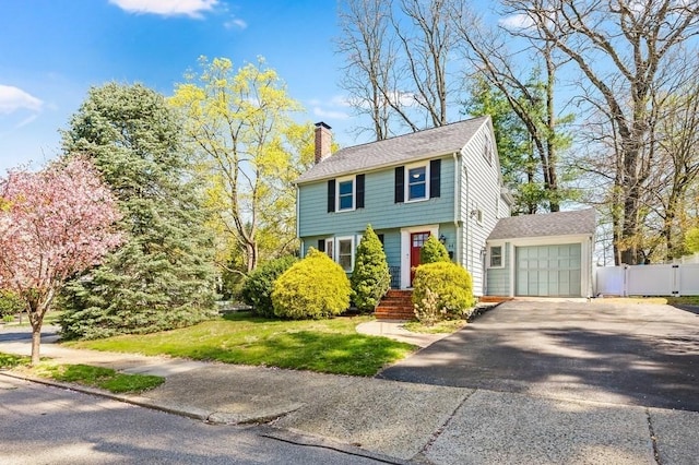 colonial house with driveway, a chimney, a garage, fence, and a front lawn