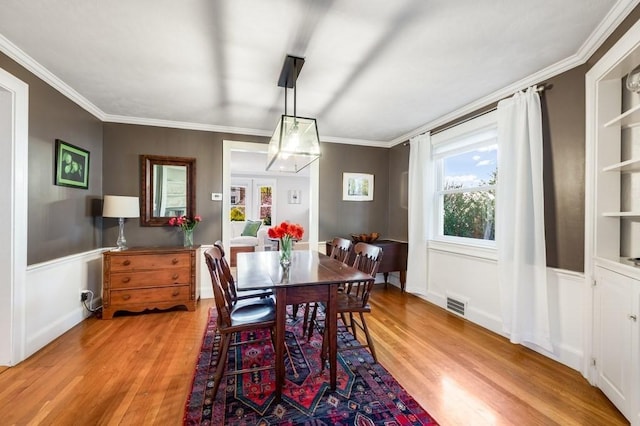 dining area with crown molding, light wood finished floors, wainscoting, and visible vents