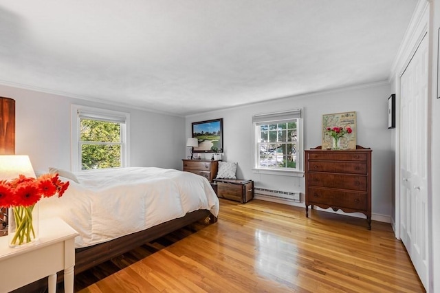 bedroom featuring a baseboard radiator, light wood-style flooring, and multiple windows