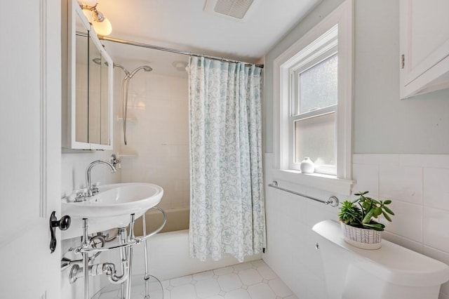 bathroom featuring toilet, visible vents, tile walls, and shower / tub combo