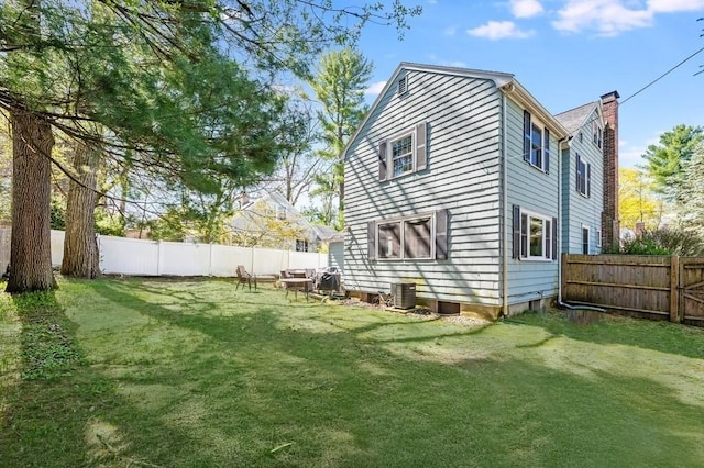 rear view of house with a fenced backyard, a chimney, a yard, and cooling unit