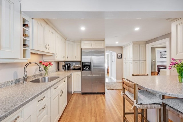 kitchen with a kitchen bar, a sink, light wood finished floors, stainless steel appliances, and white cabinetry