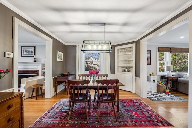 dining area featuring crown molding, built in features, light wood-style flooring, and a fireplace