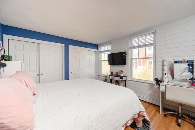 bedroom featuring multiple closets, light wood finished floors, wood walls, and a desk