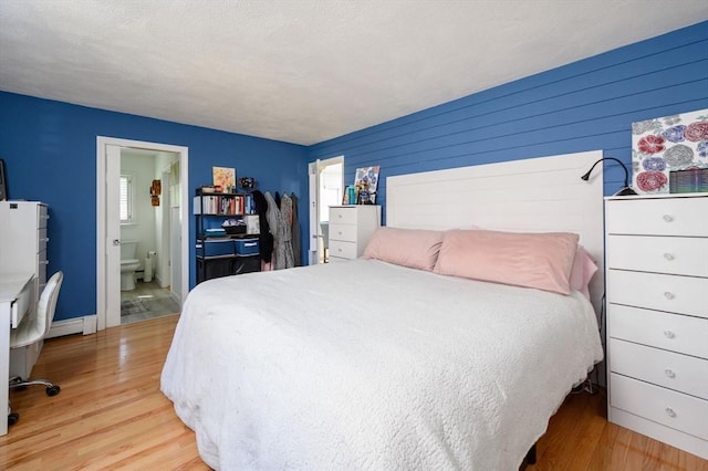 bedroom with light wood-style floors, a baseboard heating unit, ensuite bathroom, and wood walls