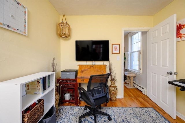 office space featuring a baseboard heating unit, wood finished floors, and baseboards
