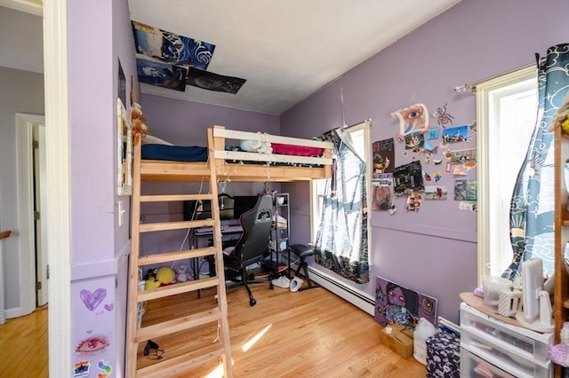 bedroom with wood finished floors, a baseboard radiator, and a desk