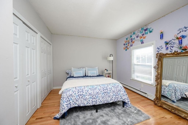bedroom with multiple closets, light wood-style floors, a baseboard heating unit, and baseboards