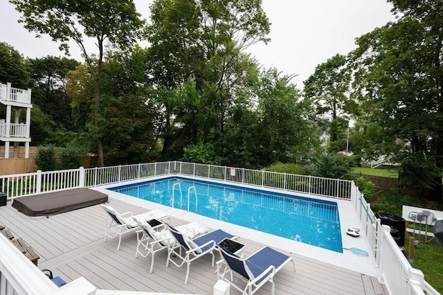 view of pool with a deck, fence, and view of wooded area