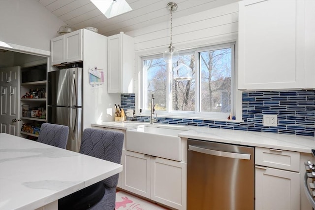 kitchen featuring stainless steel appliances, a sink, a skylight, decorative backsplash, and light stone counters