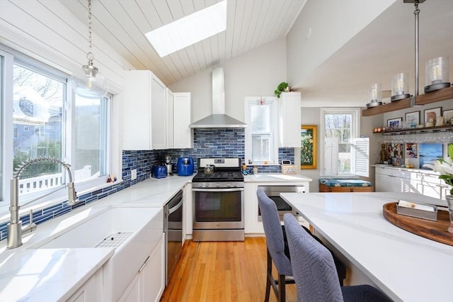 kitchen with stainless steel appliances, wall chimney exhaust hood, a sink, a skylight, and vaulted ceiling