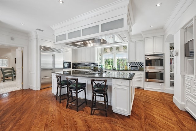 kitchen with built in appliances, tasteful backsplash, a center island, and white cabinetry