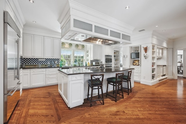 kitchen with tasteful backsplash, white cabinetry, a breakfast bar area, stainless steel built in refrigerator, and a center island with sink