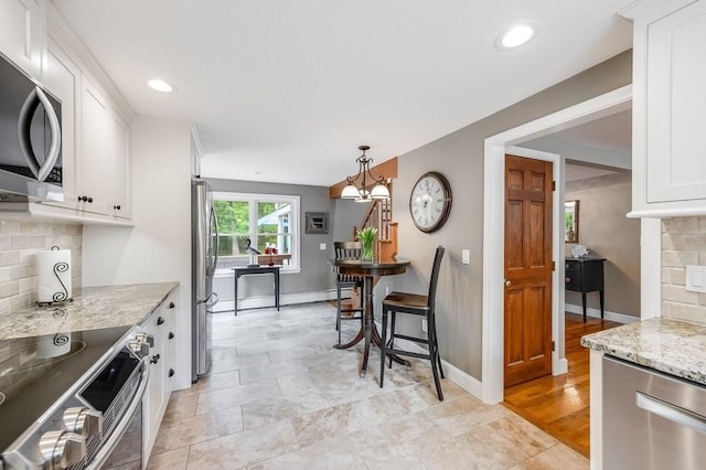 2470 W St, Wrentham, MA 02093 - kitchen featuring appliances with stainless steel finishes, white cabinetry, backsplash, light stone countertops, and baseboards