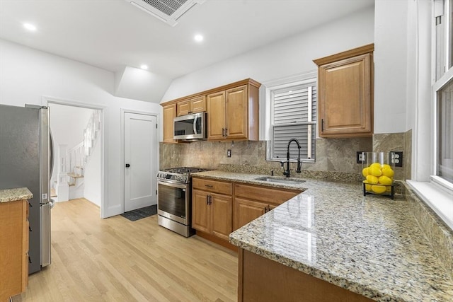 kitchen featuring light stone countertops, sink, stainless steel appliances, tasteful backsplash, and light hardwood / wood-style floors