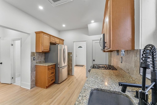 kitchen with appliances with stainless steel finishes, tasteful backsplash, light stone counters, sink, and light hardwood / wood-style flooring