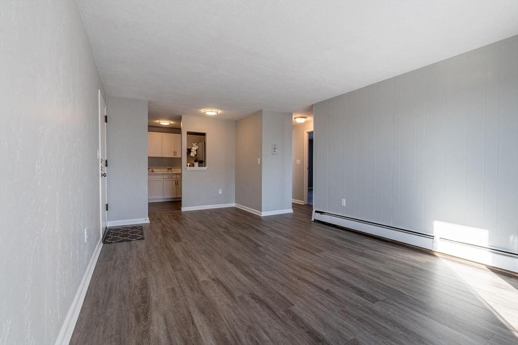 unfurnished living room featuring baseboard heating and dark hardwood / wood-style floors