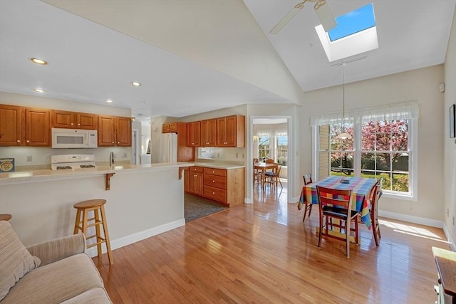 kitchen featuring plenty of natural light, a skylight, a breakfast bar, and white appliances