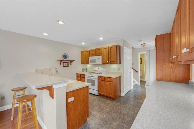 kitchen with a peninsula, white appliances, a kitchen breakfast bar, light countertops, and baseboards