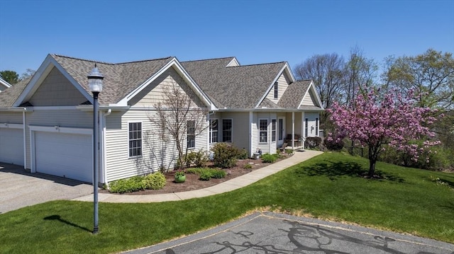 new england style home with a front yard, a shingled roof, an attached garage, and driveway