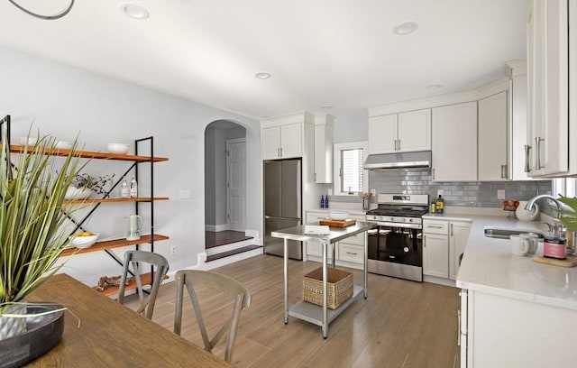 kitchen featuring arched walkways, a sink, stainless steel appliances, under cabinet range hood, and backsplash