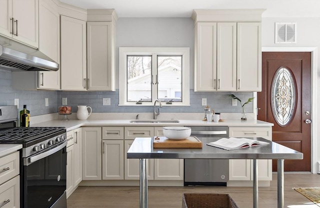 kitchen with visible vents, a sink, under cabinet range hood, appliances with stainless steel finishes, and light countertops