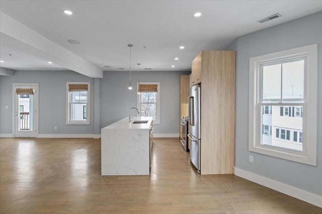 kitchen with a center island with sink, sink, pendant lighting, high end fridge, and light hardwood / wood-style floors