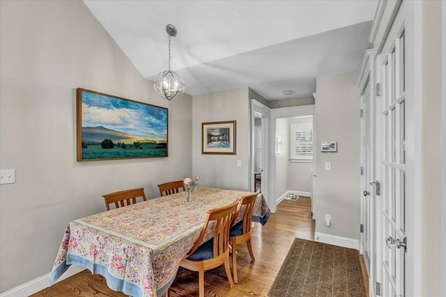 dining space with vaulted ceiling, an inviting chandelier, and hardwood / wood-style floors